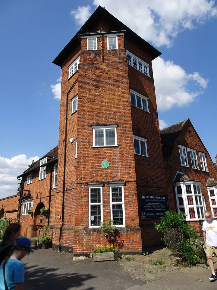 The red-brick tower of the Brentham Club clubhouse on Meadvale Road, with the club's noticeboard and a green Fred Perry plaque